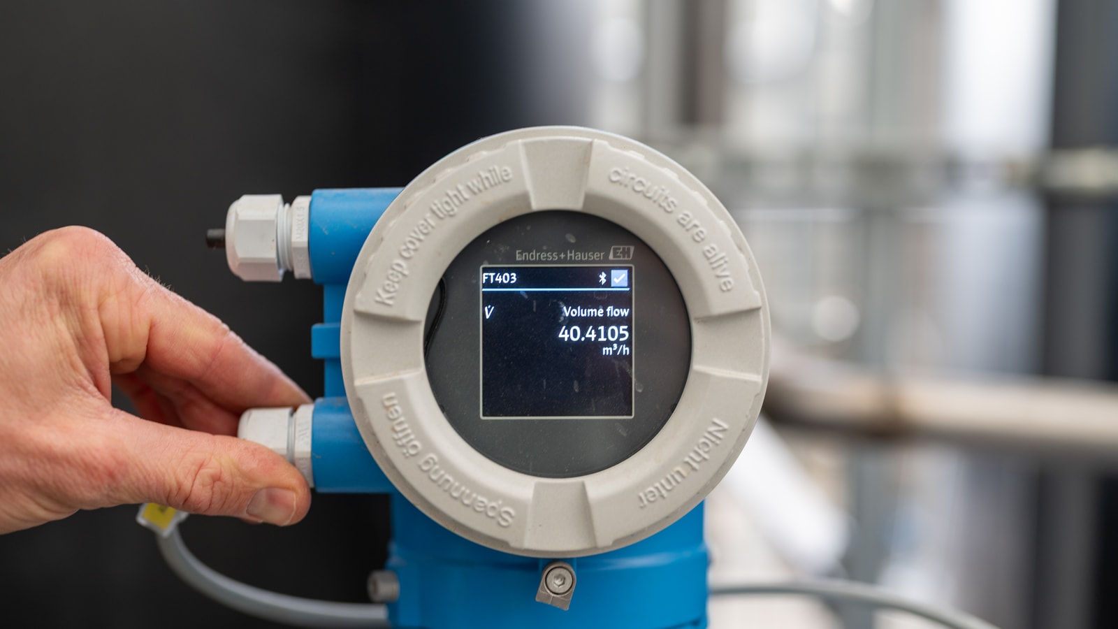 A flow meter transmitter on a process line, its display reading a volume flow in cubic metres an hour