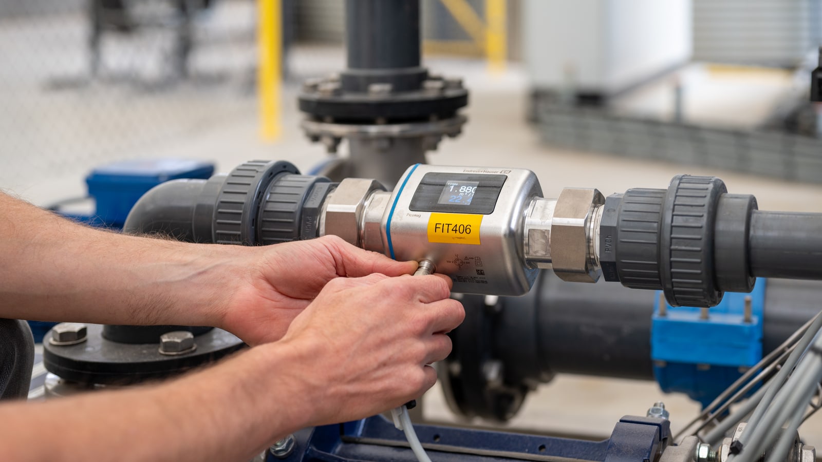 Hands wiring a magnetic flow meter tagged FIT406 into a pump skid