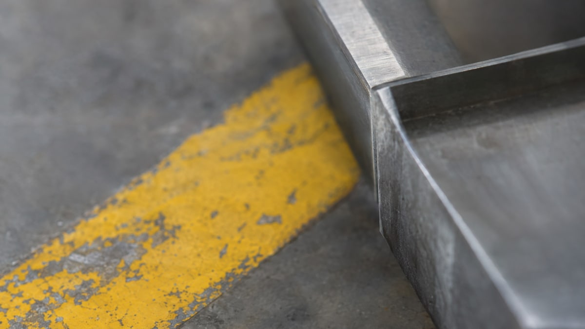 An abstract study: machined metal edges crossing a worn yellow stripe in daylight